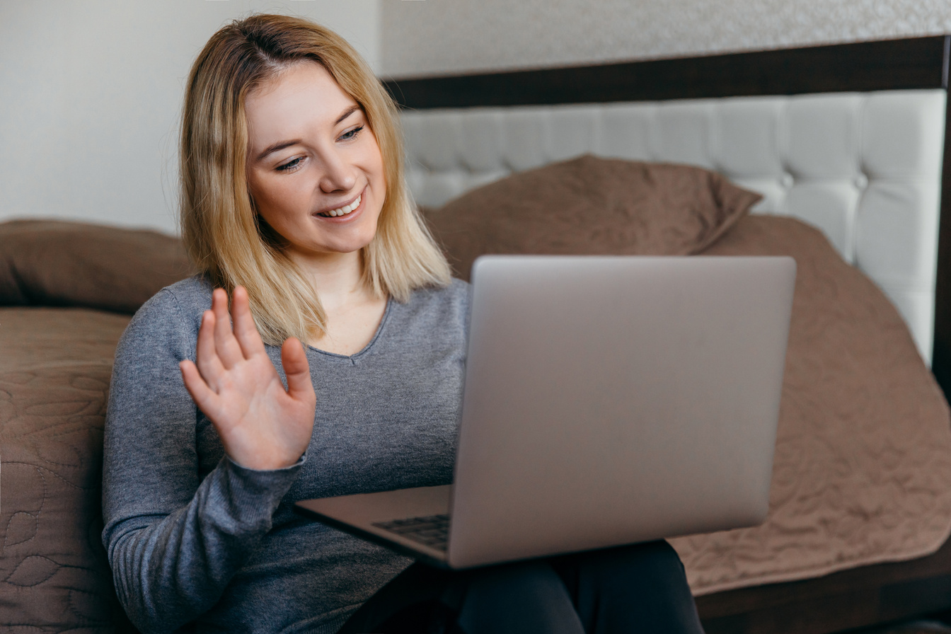 Woman sitting on the floor in bedroom and having Zoom video conference call via computer withfriend. Zoom Call Meeting. Home as hub during Coronavirus pandemic